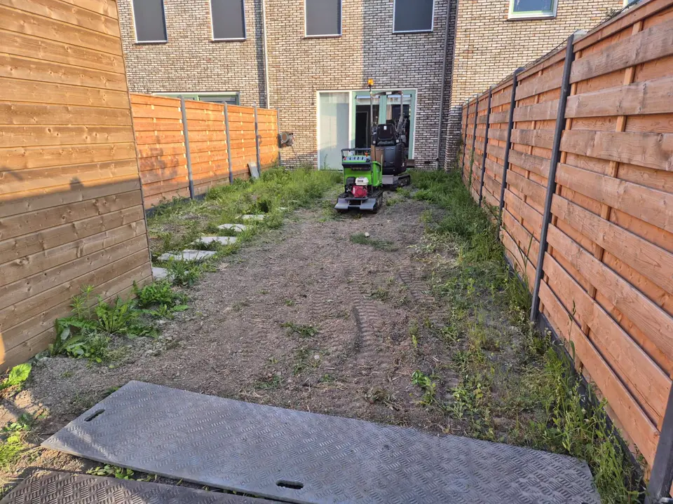 Kale achtertuin met rijplaten, een minigraver staat bij het huis klaar