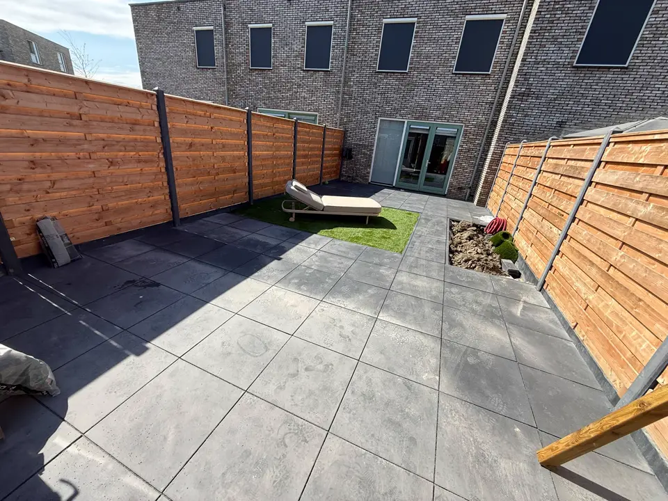 Nieuw terras met grote tegels, grasvlak en ligbed, richting het huis