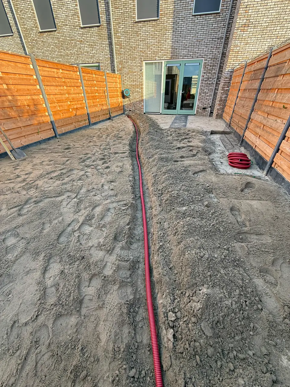 Vlak zandbed met een rode leiding door de tuin